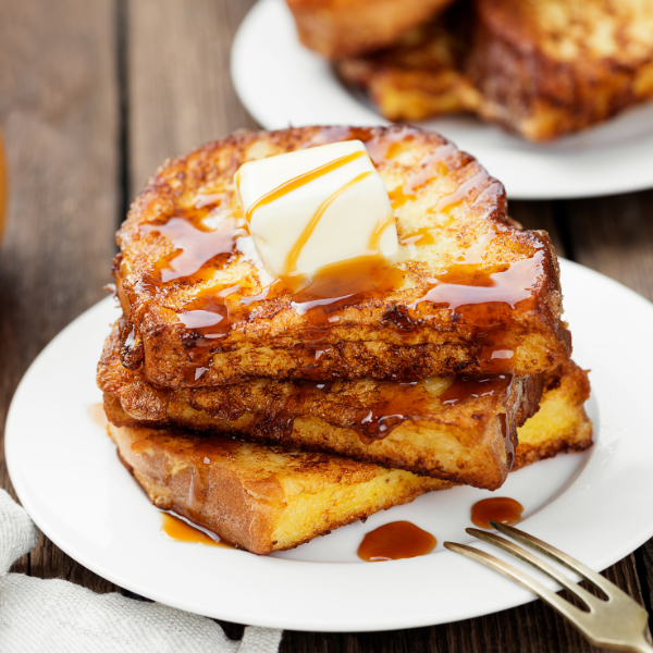 Slices of french toast stacked on a small plate, drizzled with syrup and knob of butter