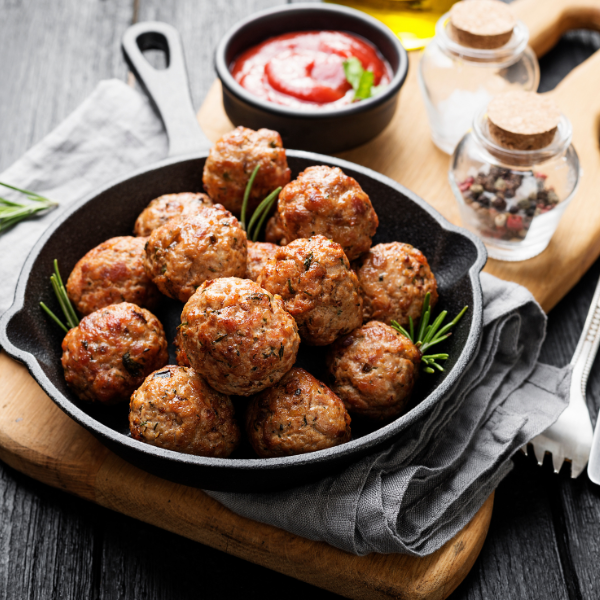 Shallow cast iron pan with pile of meatballs sitting on wooden slab