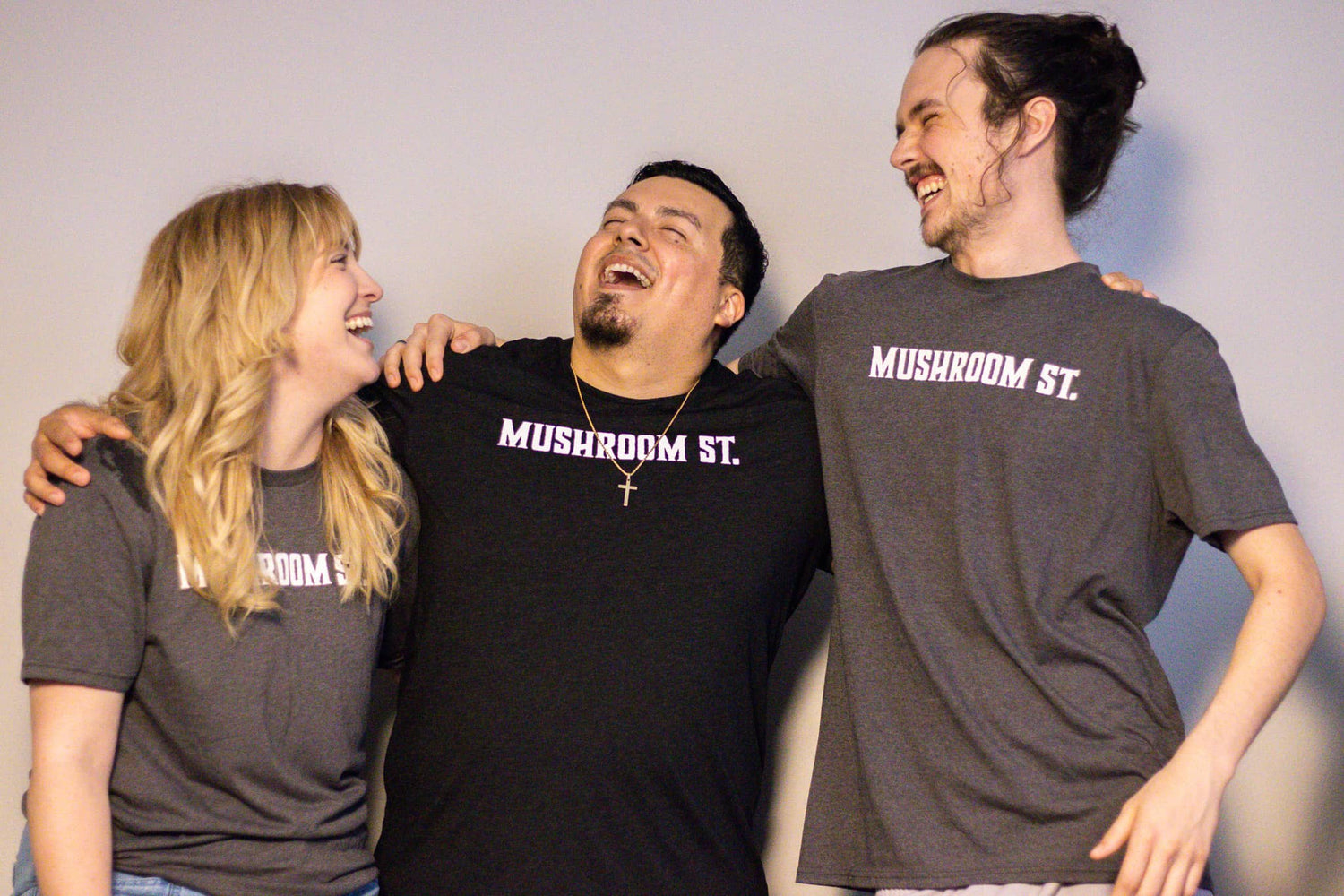 Sophie, Alejandro, and Christian smiling together wearing Mushroom Street shirts