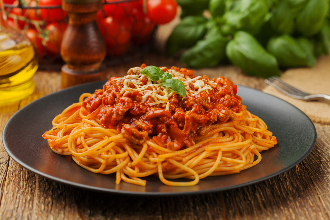 Plate of spaghetti garnished with basil on wooden table