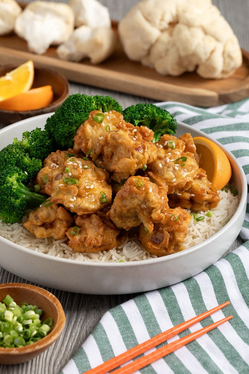 Bowl of orange-glazed lion's mane over rice with broccoli, spring onion and orange wedges