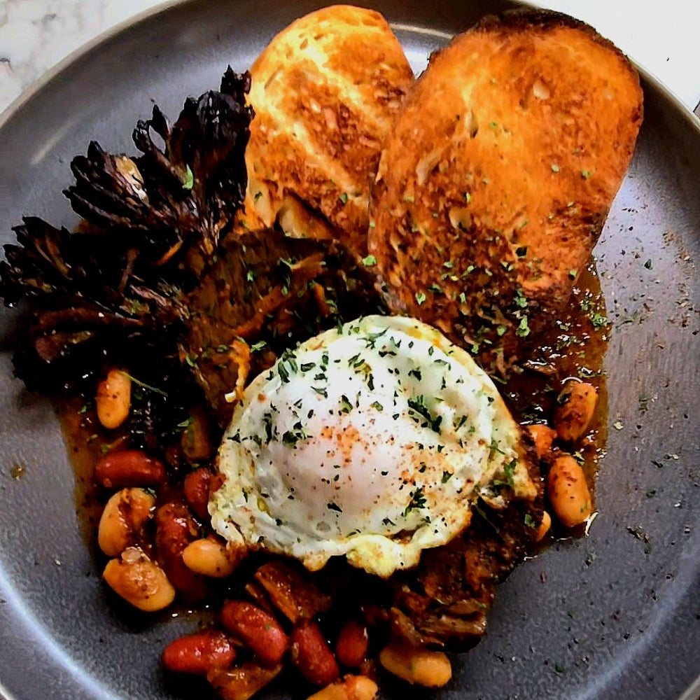 Plate of braised beef with a fried egg, beans, roasted maitake and toasted bread