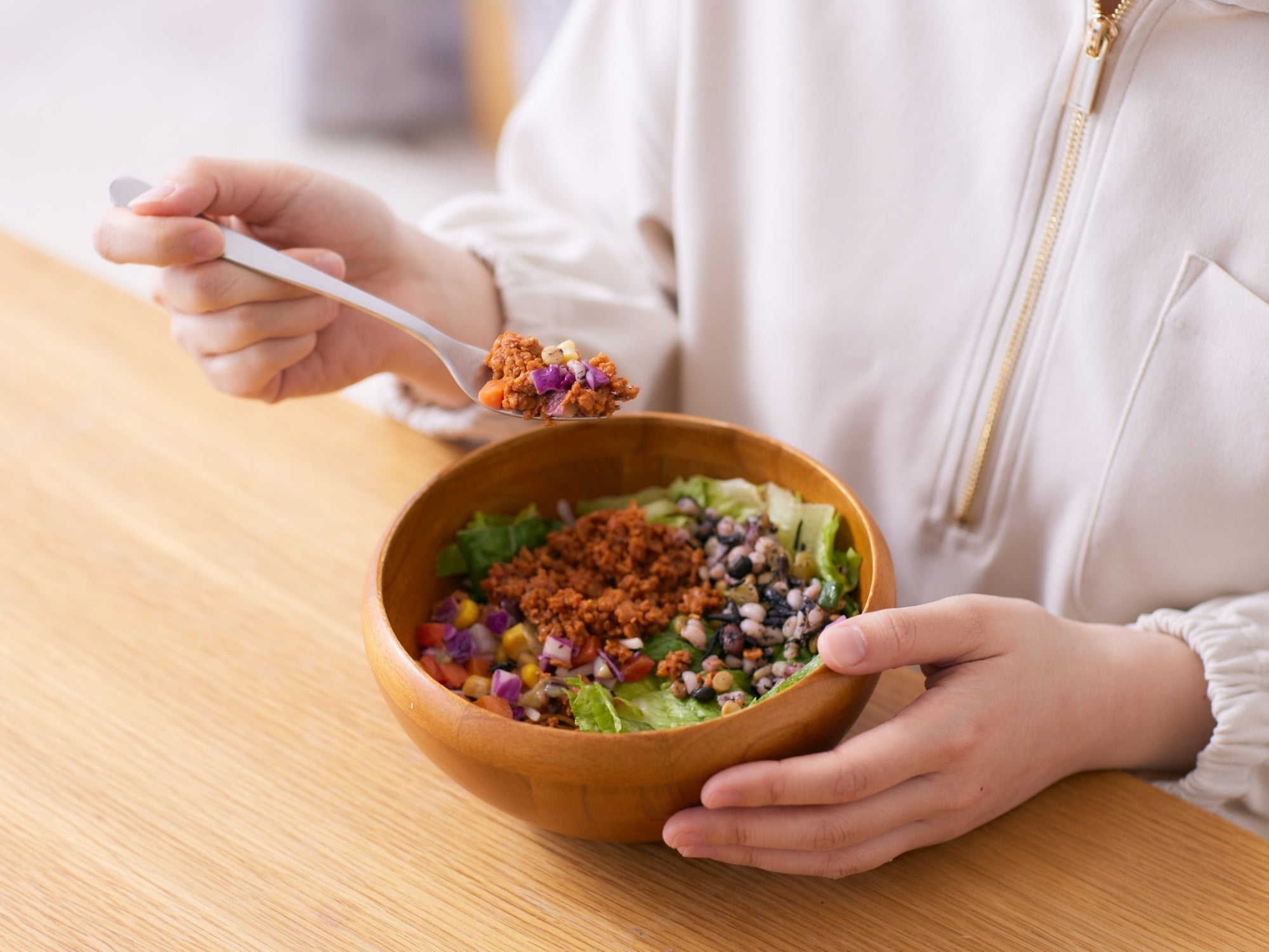 Person eating a wooden bowl of grain salad with greens and mushrooms