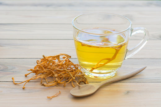 Glass cup of golden cordyceps tea beside a wooden spoon of dried cordyceps