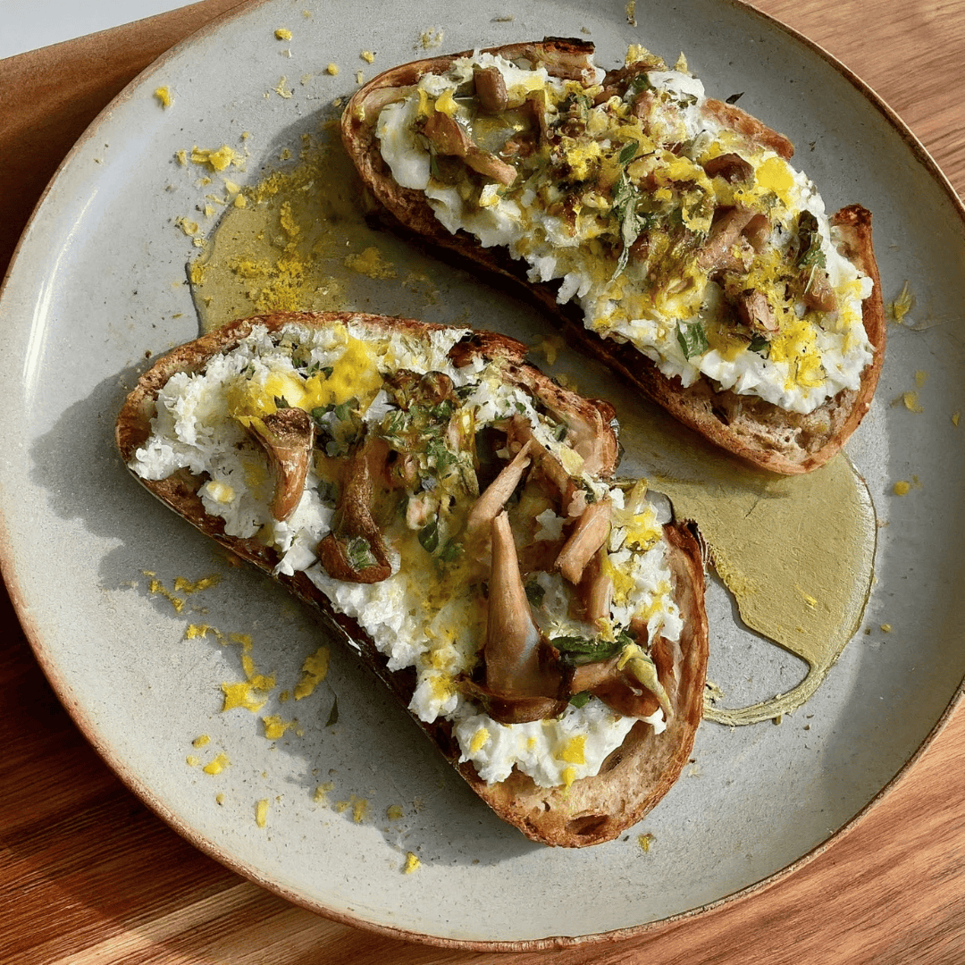 Two slices of sourdough toast with herbed ricotta, sautéed mushrooms and lemon zest