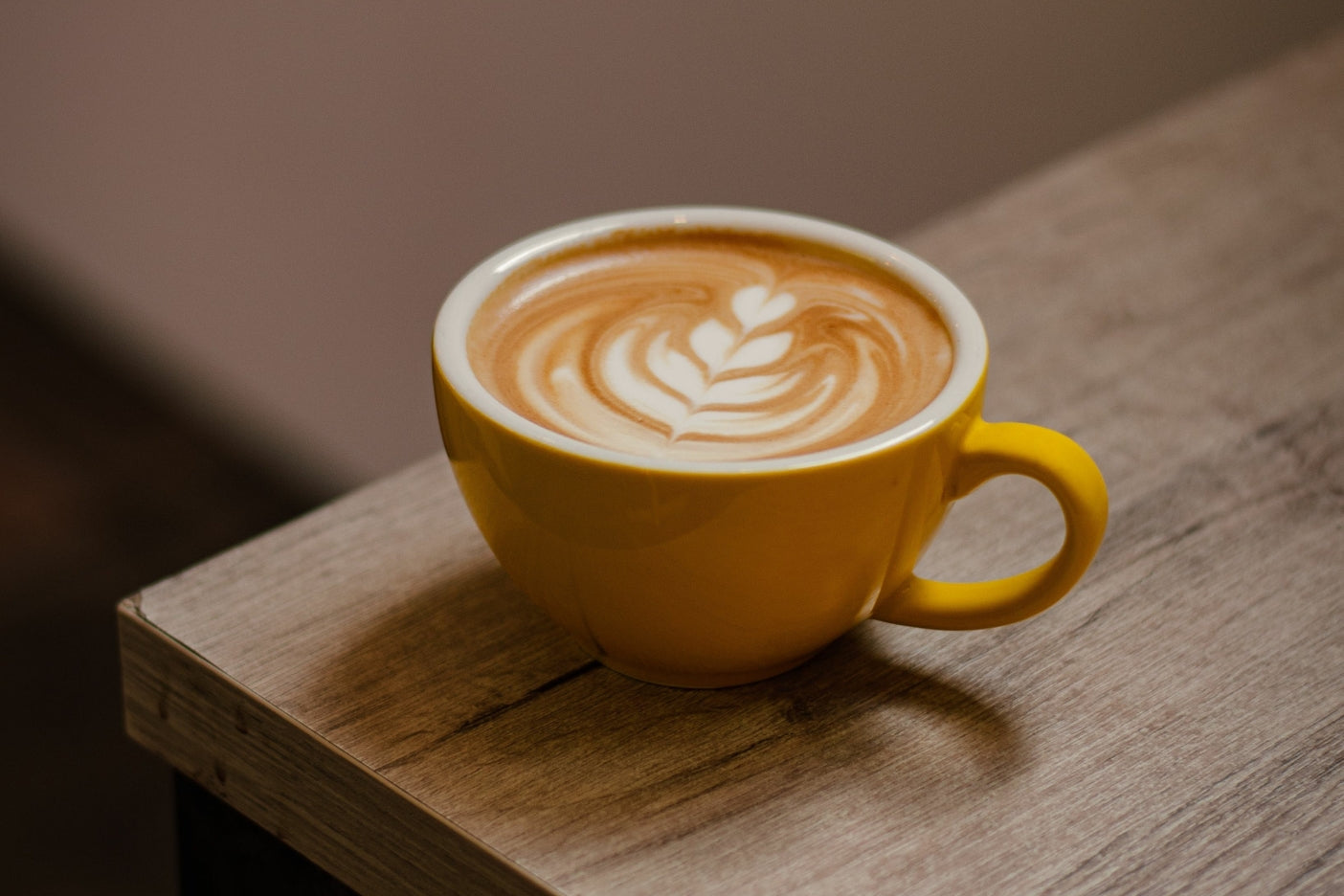 Yellow ceramic cup of latte with leaf latte art on a wooden table