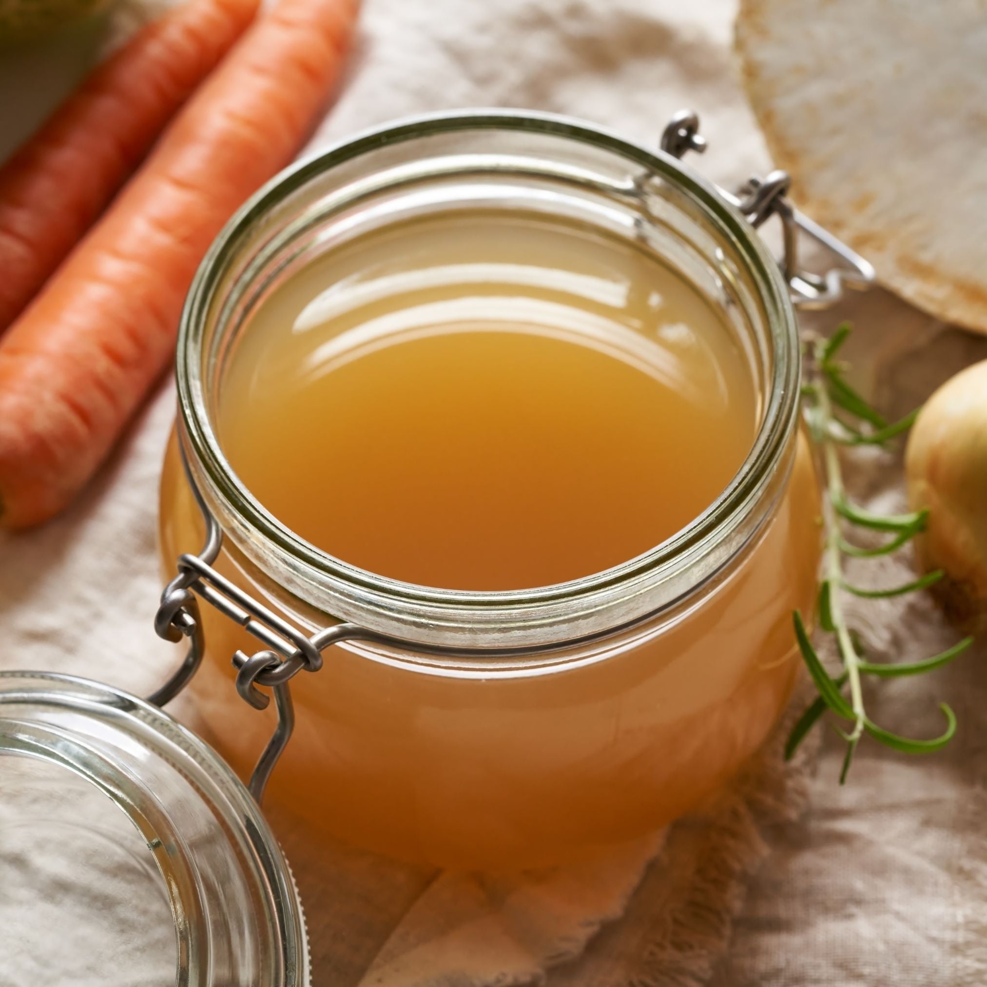 Clasp-top jar of golden mushroom broth beside carrots and onion