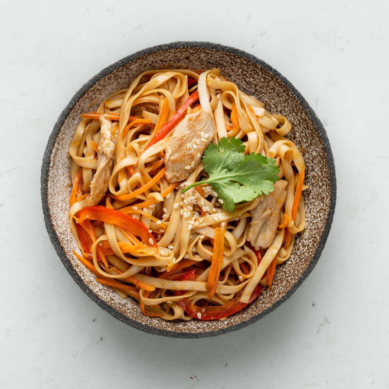 Bowl of mushroom noodle stir fry with peppers, carrot and coriander