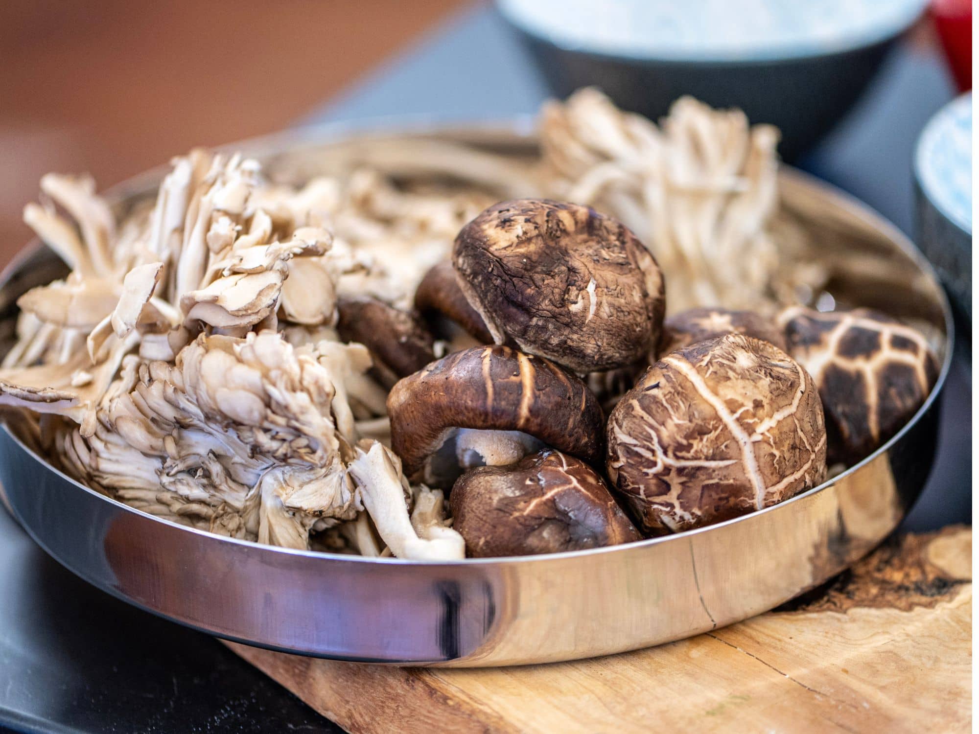 Metal tray of fresh shiitake and oyster mushrooms on a wooden board