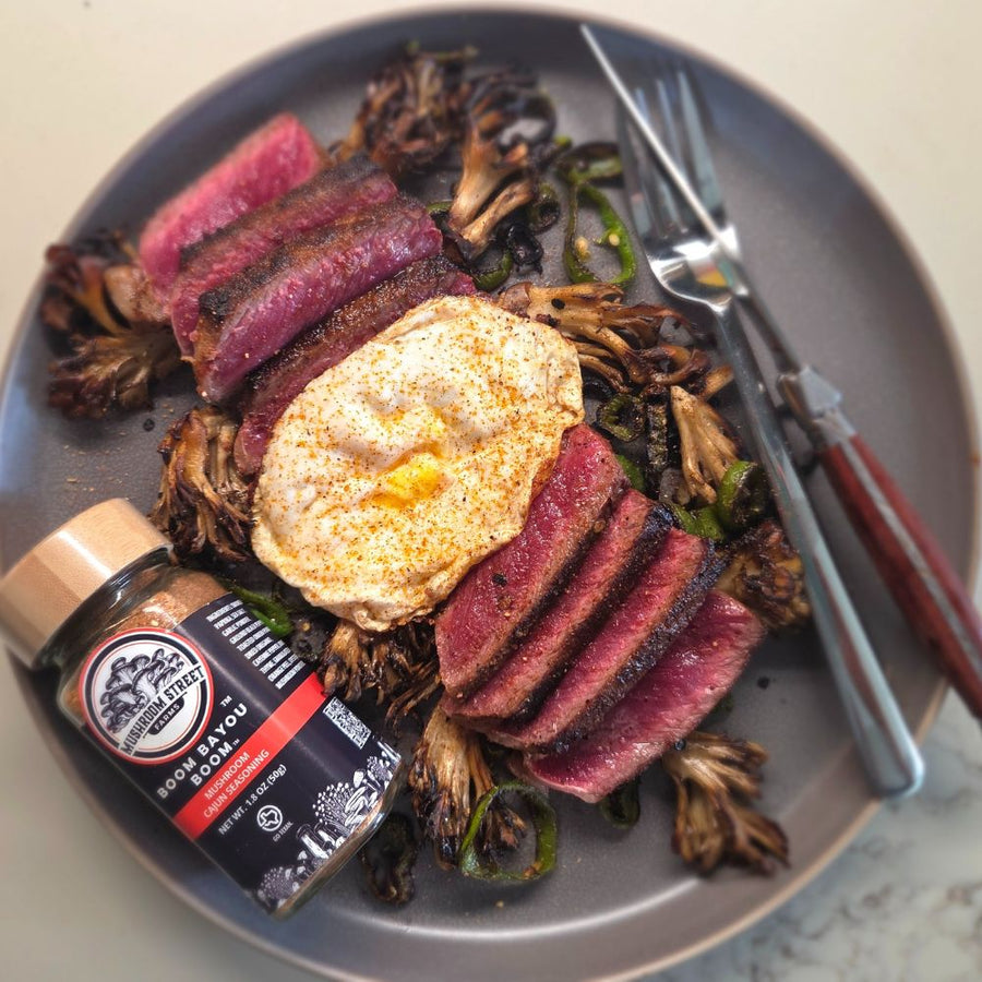 Plate of sliced steak with a fried egg and roasted maitake, beside a jar of Mushroom Street Farms Cajun seasoning
