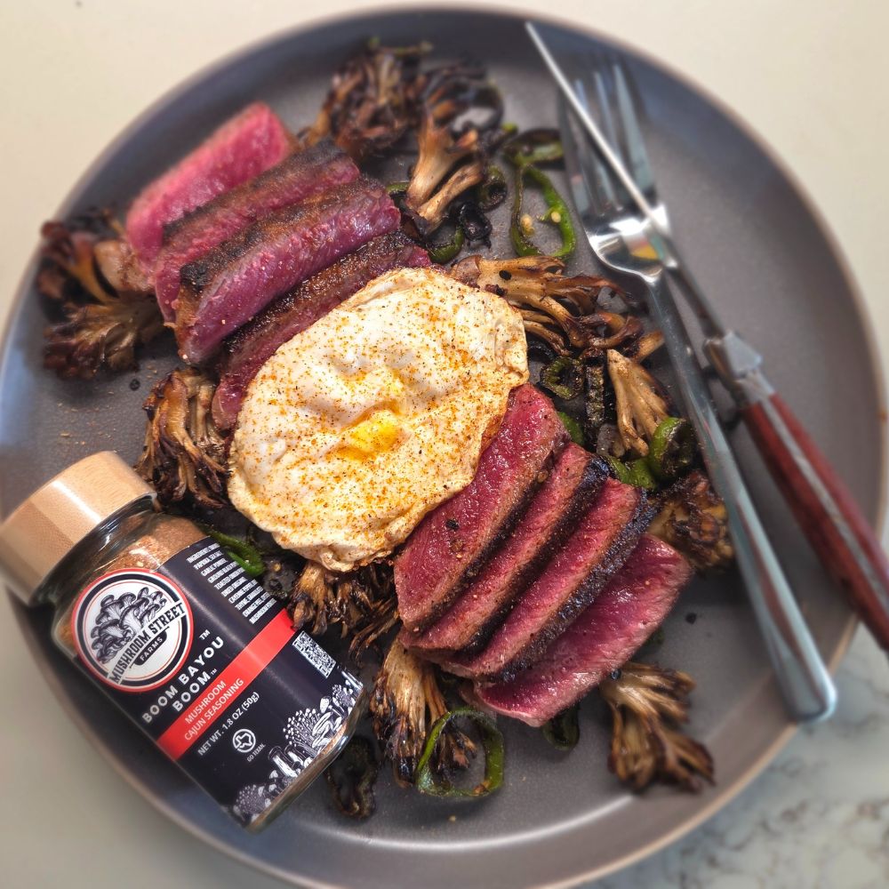 Plate of sliced steak with a fried egg and roasted maitake, beside a jar of Mushroom Street Farms Cajun seasoning
