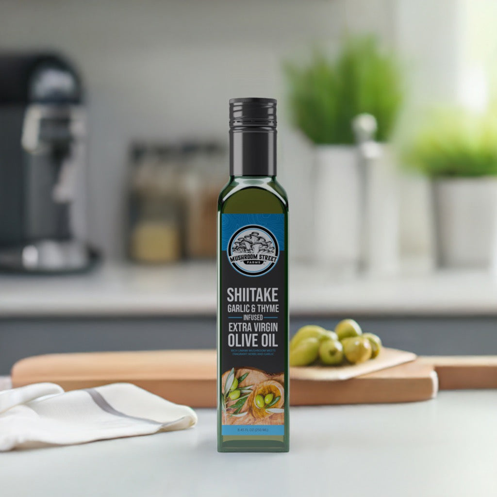 Bottle of shiitake, sage and thyme infused olive oil on a kitchen counter beside a cutting board and green olives